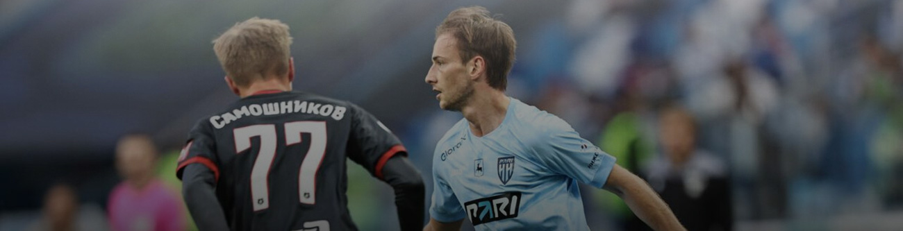 На изображении двое футболистов на поле: один в черной форме с номером 77, другой в светло-голубой форме. Их окружает размытая публика или коллеги на трибунах. Игроки сконцентрированы на игре